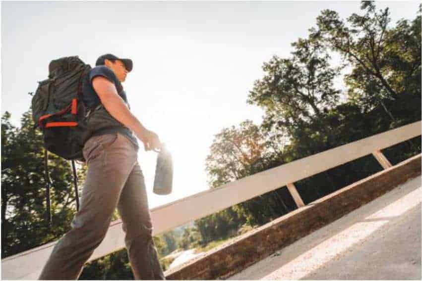 man walking over bridge with backpack holding a grizzly grip bottle