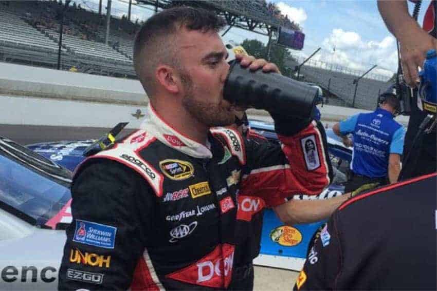 race car driver drinking from grizzly grip cup with track in background