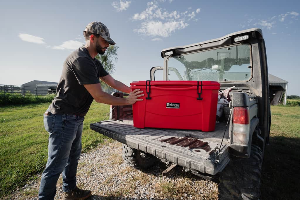 grizzly 60 cooler, red. sitting in back of truck with tailgate down in the country